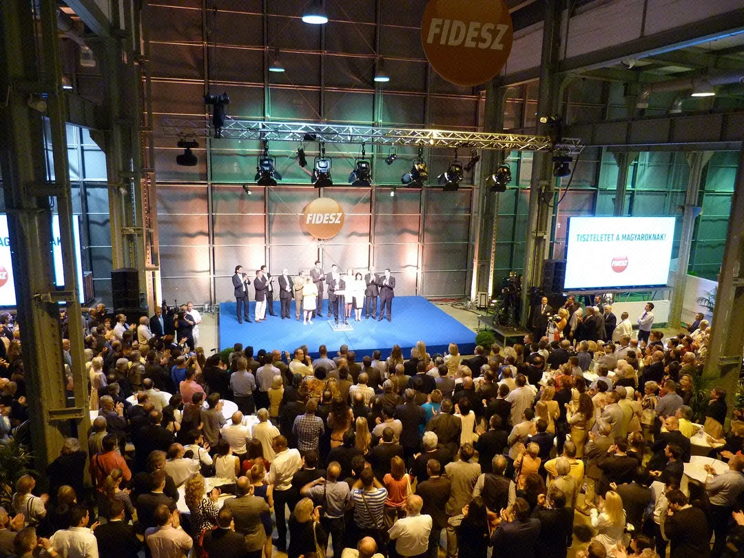 Menschen stehen dicht gedrängt in einer Halle bei einer Fidesz-Wahlveranstaltung zur Europawahl 2014 in Budapest, im Hintergrund sind Leinwände und Bühnenbeleuchtung zu sehen.